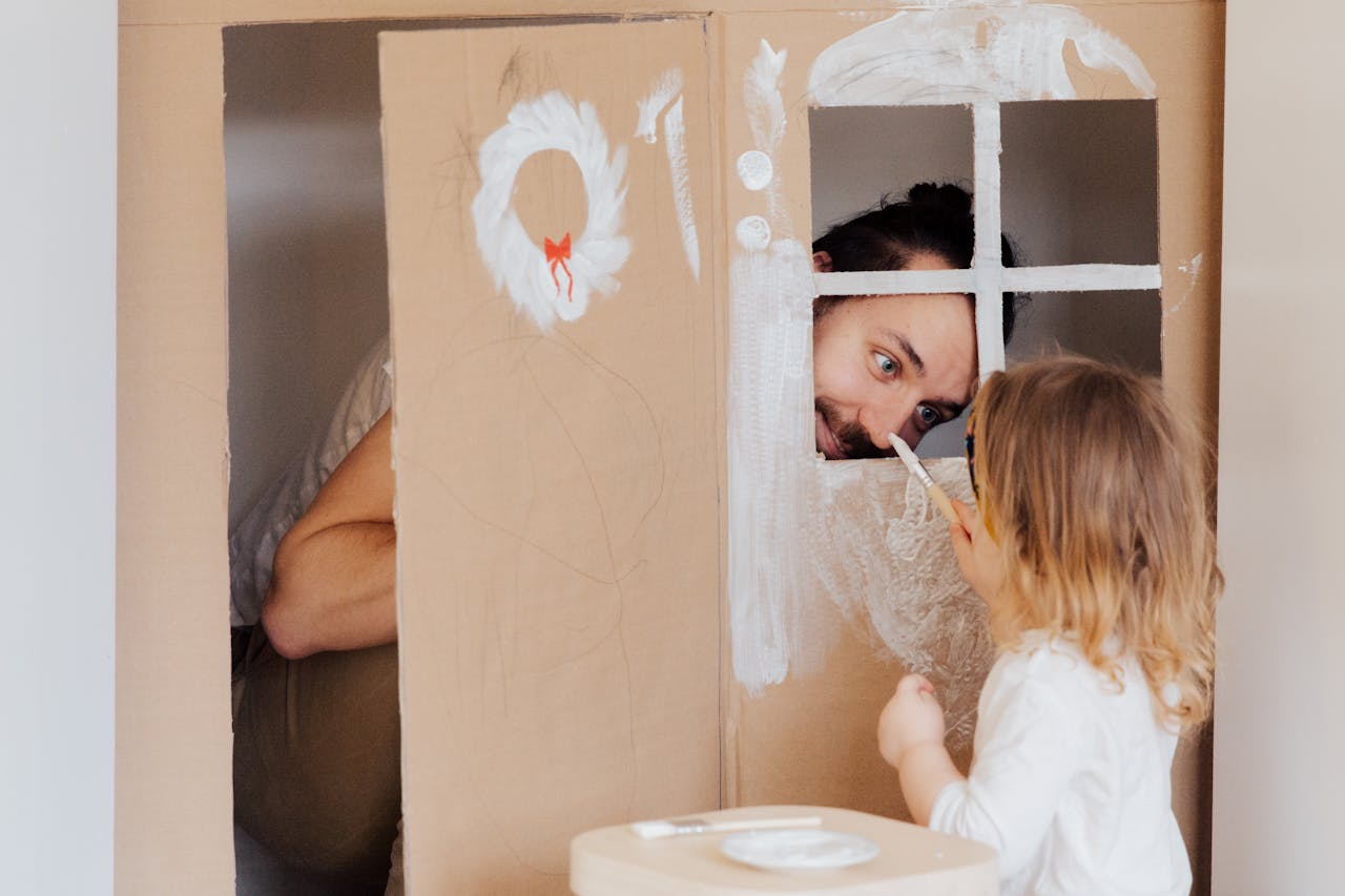 experience-02 Father and daughter enjoying creative bonding by painting a cardboard playhouse indoors.