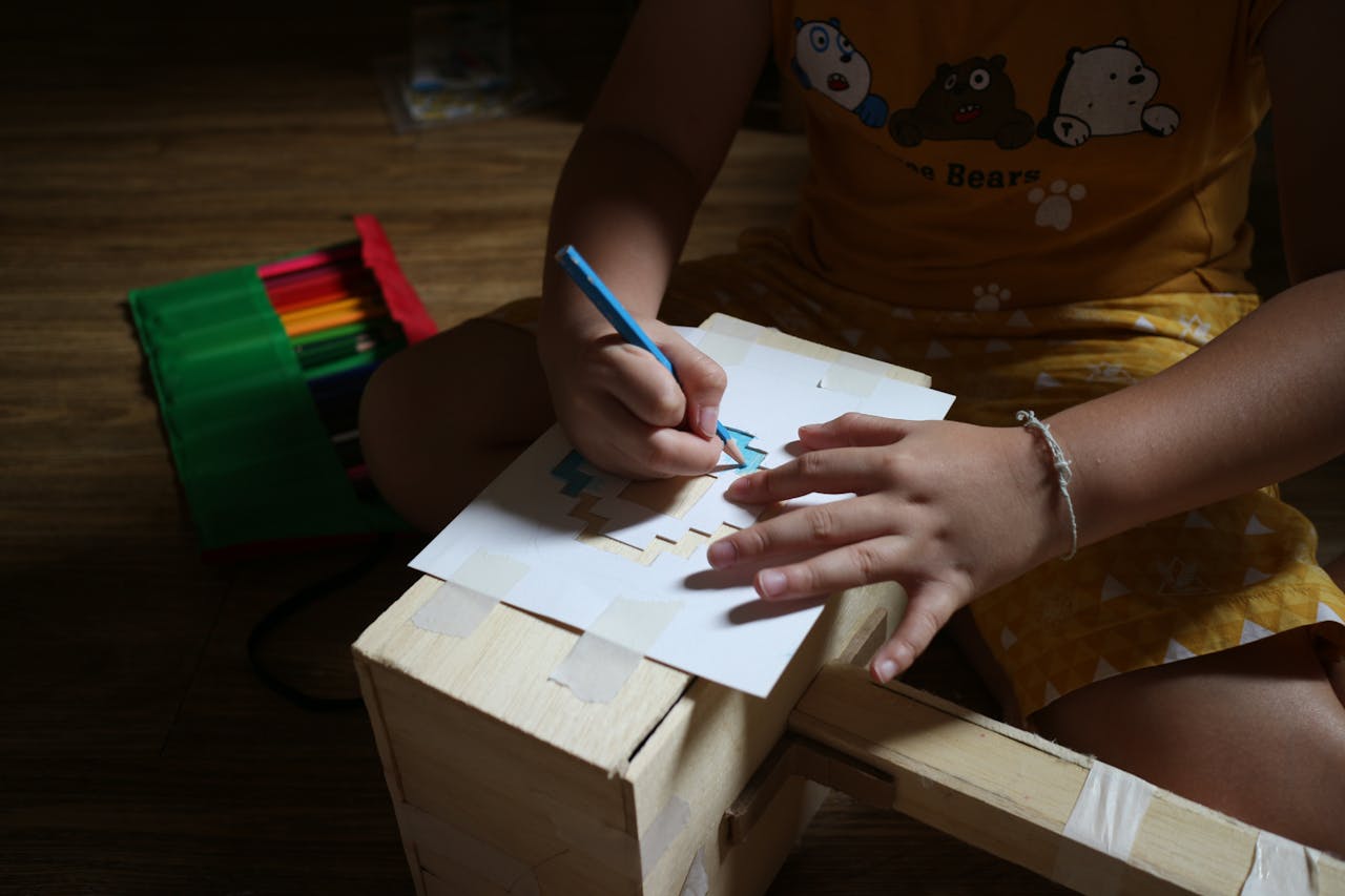 A child creatively draws using colored pencils on a wooden box, showcasing home creativity.